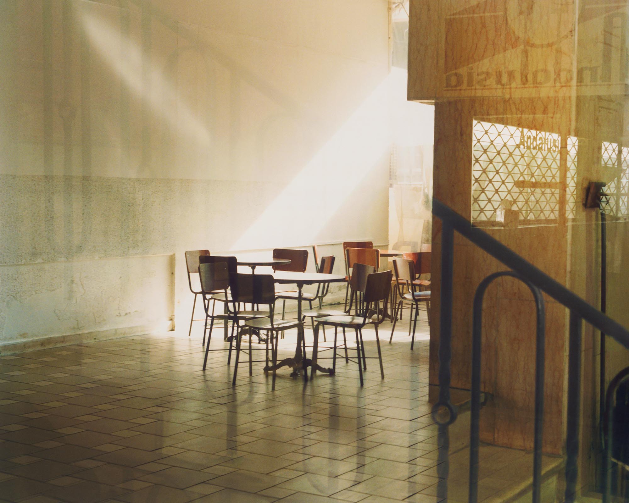 http://Tables%20and%20chairs%20in%20sunlit%20space,%20gold%20light%20from%20windows%20and%20relections.